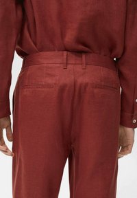 Red linen pants featuring a tailored fit, flat front, and two back pockets. Texture appears smooth with fine stitching details.