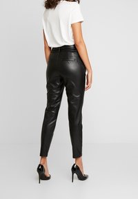 Schwarze Kunstlederhosen mit enger Passform, hoher Taille und Gesäßtaschen, kombiniert mit einem weißen T-Shirt und schwarzen hohen Schuhen.