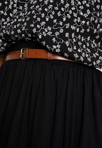 Svart kjol med plisserad textur, ihopparad med en blommönstrad svart och vit blus samt ett brunt läderbälte med en metallspänne.