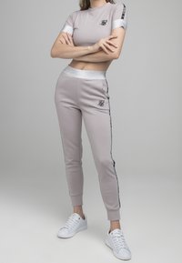Conjunto deportivo a juego en gris claro, hecho de material suave. Top de manga corta con acentos plateados y logotipo; pantalones ajustados con rayas laterales negras.