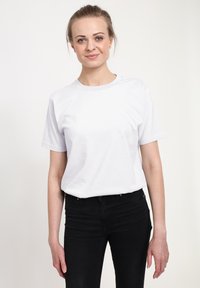 Bílý bavlněný tričko s krátkými rukávy, kulatým výstřihem a volným střihem, spárované s černými džíny. Jednoduchý design, žádné viditelné grafiky nebo vzory.