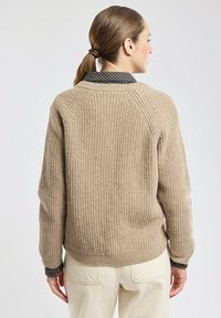 Beige geribd sweater met een ronde hals en raglanmouwen. Heeft een geblokte donkere kraag. Comfortabele brei-textuur.