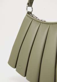 Pleated olive green leather handbag with silver hardware. Features a zip closure and embossed logo. Compact, with a structured design.