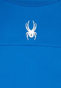 Logo de araña blanca centrado en un fondo de tela azul brillante y homogéneo con costuras horizontales cerca de la parte superior.