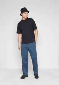 Black cotton t-shirt, loose-fit blue trousers, black bucket hat, and black shoes. Simple design, no visible patterns or accents.