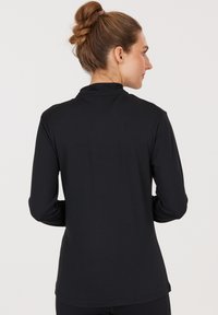 Black long-sleeve shirt made from smooth, lightweight fabric. Features a high collar and a fitted design with a curved hem at the back.