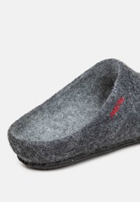 Pantofole grigie in feltro con una forma liscia e arrotondata. Presentano un esterno morbido e testurizzato e un dettaglio con logo rosso. Suola piatta con design minimalista.