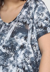 Camiseta de manga corta en azul marino y blanco, con un patrón abstracto parecido a nubes y un diseño de escote en V, fabricada con un tejido suave y transpirable.