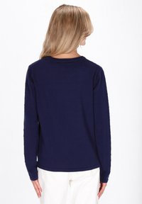 Pull à manches longues bleu marine avec motifs torsadés texturés sur les manches, col rond, coupe décontractée, porté avec un pantalon de couleur claire.