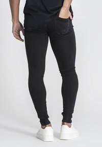 Mustat kapeat farkut, joissa on klassinen viisi-taskuinen muotoilu ja lievää haalistumista. Yhdistettynä valkoisiin lenkkareihin.