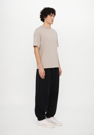 Light taupe short-sleeve t-shirt paired with loose-fitting black sweatpants and white sneakers, featuring a relaxed design and soft fabric.
