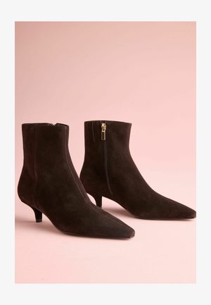 Fekete velúr bokacsizmák hegyes orral, oldalsó zipzárral, arany színű fémrészekkel és kis sarkakkal. Sima felület és letisztult dizájn.