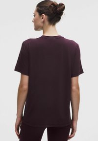 Burgundia lühikeste varrukate ja ümmarguse kaelusega t-särk, sujuva tekstuuriga ja veidi vabam sobivus, hem, mis ulatub veidi ülespoole vööst.