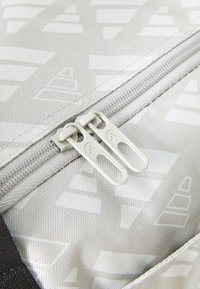 Bolso de tela gris con patrones geométricos, presenta un doble cierre con tiradores curvados y detalles acentuados texturizados.