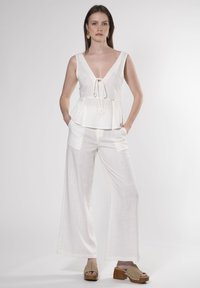 Top peplum bianco in lino con scollatura a V profonda e cordoncino; abbinato a pantaloni larghi bianchi in lino. Indossato con zoccoli beige con piattaforma.