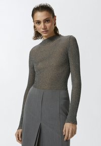 Siva rebrasta majica dugih rukava s visokim izrezom i blagim sjajem, u kombinaciji s pripijenom sivom suknjom s prednjim prorezom i bočnom džepom.