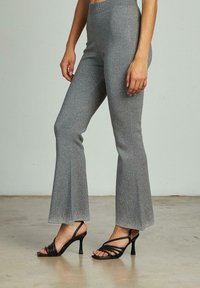 Grijze flared broeken met een metallic glans, voorzien van een hoge tailleband en textielstof. Gecombineerd met zwarte sandalen met hoge hakken en bandjes.