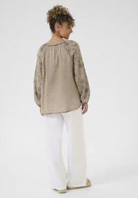 Bluză cu mânecă lungă din in bej, cu țesătură texturată și model floral, asortată cu pantaloni albaștri largi și sandale espadrile.