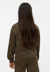 Pealetrükiga pusa elastsete varrukaservadega, valmistatud pehmest kangast. Pikk, tume juuksed voolavad selja peale. Kandes sobivaid pükse.