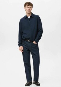 Dark blue long-sleeve polo shirt with a collared neckline, paired with dark denim jeans. The outfit features a slim fit and minimal design.