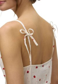 Vestido de verano blanco con estampado de fresas rojas, tirantes finos con lazos y una textura de tela de ajuste relajado, que exhibe un diseño de espalda descubierta.