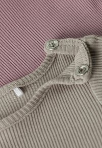 Tissu côtelé en lavande atténuée et gris clair, avec un col boutonné. Motif texturé avec des couleurs contrastantes et des pressions métalliques.