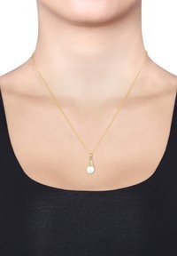 Guld kæde halskæde med en hvid perle vedhæng og dekorativt accent. Designet er slankt, moderne og minimalistisk.