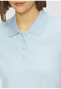 Lichtblauwe polo met een zachte textuur, geribbelde kraag en knoopsluiting met drie knopen, ontworpen voor een comfortabele pasvorm en een casual look.