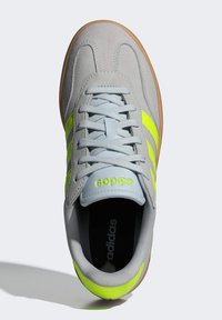 Gray suede athletic shoe with bright yellow accents, featuring a lace-up design, curved lines, and a textured sole.