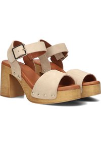 Beige suede sandalen met hakken in blokhout, verstelbare enkelband en metalen studs aan de voorkant. Open teen design.