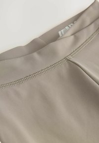 Ceinture en tissu beige avec une texture lisse ; présente des coutures plates et un léger éclat ; bord replié visible.