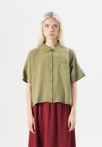 Korte mouwen, olijfgroene cropped jack met een rits aan de voorkant, puntige kraag en een borstzak, gecombineerd met een lange bordeauxrode rok.