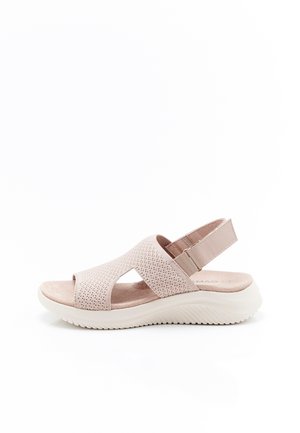 Beige Sandale mit offenem Zehenbereich, atmungsaktivem Strickoberteil, gepolsterter Sohle und verstellbarem Klettverschluss vor weißem Hintergrund.