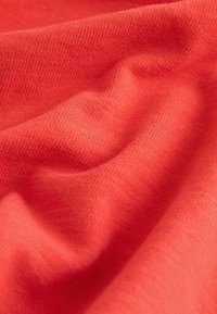 Tessuto lavorato a maglia in morbido e testurizzato colore corallo-arancio, con pieghe delicate e un aspetto liscio e accogliente.