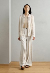 Lys beige knappopp cardigan over en kremfarget topp, sammen med brede stripete bukser. Glatt tekstur, avslappet passform og minimalistisk design.