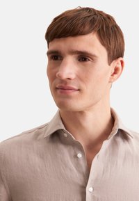 Lichtbeige linnen shirt met een klassieke kraag, voorzien van subtiele textuur en drie knopen bij de hals. Glad stof met een relaxte pasvorm.