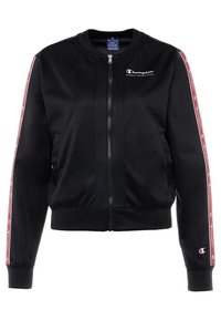 Svart atletisk jacka med dragkedja framtill, ribbade ärmslut och röda sidosträck med upprepad branding. Mjuk, slät material med fickor.