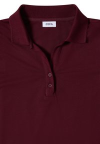 Polo bordeaux avec col, deux boutons sur la patte de boutonnage et une étiquette de marque "CECIL" à l'intérieur du col.