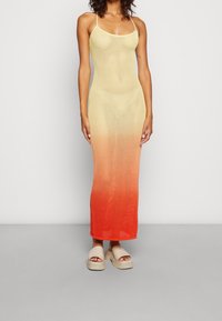 Strick-Maxikleid mit Spaghettiträgern, das einen Farbverlauf von Gelb zu Orange aufweist, hergestellt aus offen gewebtem Material. Glatte Textur, figurbetonte Form.