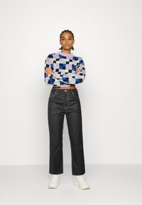 Sweater curta multicolorido com padrão xadrez em roxo, azul, preto e menta; combinado com jeans pretos de cintura alta e ténis brancos.