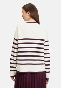 Pull blanc avec de larges rayures bordeaux, présentant un col rond et des poignets côtelés, associé à une jupe superposée en tulle bordeaux.