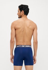 Marineblå boxer shorts lavet af glat stof med en grå Nike-logo talje. Har et tætsiddende design og midt-lår længde.