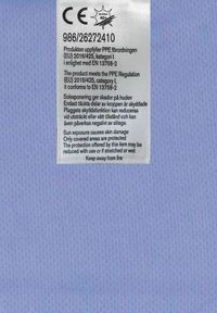 Vitt etikett på ljusblå texturerad tyg, som visar skötselråd och efterlevnadsinformation. Inkluderar CE-märke och varning för solutsättning.