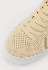  Bézs kötött sneaker textúrált hálós felsőrésszel, lapos fűzőkkel és fehér gumitalppal. SimáT orr rész és légáteresztő kialakítás jellemzi.