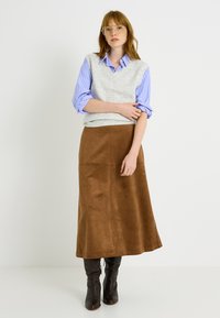 Chaleco gris de punto sobre una camisa azul de rayas, combinado con una falda maxi de ante marrón y botas negras hasta la rodilla. Acento sencillo con un anillo.