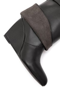 Botte noire en cuir à mi-mollet avec un revers en daim gris, talon compensé et texture lisse, présentant des lignes de design courbées et des détails de couture subtils.