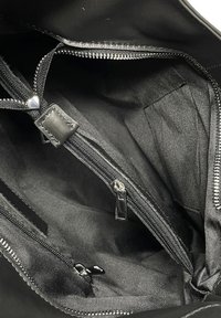 Wnętrze czarnej skórzanej torby, z wieloma czarnymi materiałowymi kieszeniami, suwakami i gładką, matową fakturą. Detalami są srebrne akcesoria.