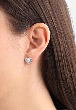 Pendientes de stud con forma de corazón en metal plateado, que presentan una superficie texturizada y acentos de piedras claras, exhibiendo un acabado pulido y un diseño compacto.