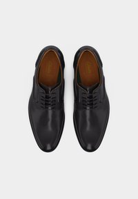 Ζευγάρι μαύρα δερμάτινα επίσημα παπούτσια ανδρικά με κορδόνια, ορατά από πάνω σε απλό λευκό φόντο.