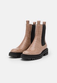 Bottes Chelsea en faux cuir marron avec une texture crocodile, panneaux latéraux élastiques noirs et semelles épaisses noires. Deux languettes à l'arrière pour un enfilage facile.